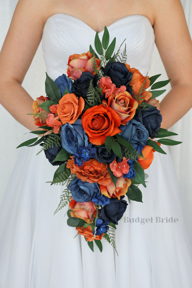 Bouquet with orange and blue flowers held by a person wearing a white dress.